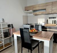 A kitchen in a studio apartment with a wooden decor, a dining table, and a bookshelf.