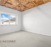 A room with a window, bare ceiling, and exposed concrete in a family house.