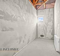 Unfinished room, with gray plaster on the walls, a small window, and visible roof structure.