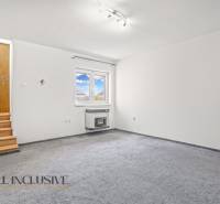 White room with carpeted floor, wooden stairs, and a wall with a window in a family house.