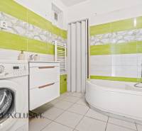 A bathroom in a family house with a bathtub, washing machine, and green tiles.