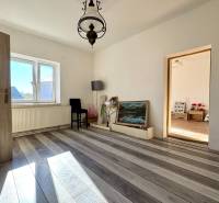 A room in a family house with white walls, a wooden decor floor, and a large window.