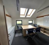 An office with a wooden floor design, skylights, and tables with chairs.