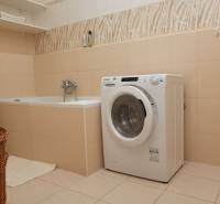 A bathroom with a bathtub, washing machine, and shelf in a 2-room apartment.