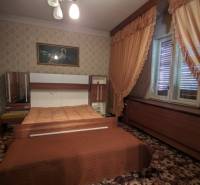 A bedroom in a family house with a carpet, furniture, and curtains in shades of brown.