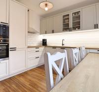 A kitchen in a 3-room apartment with a wooden decor floor and white kitchen cabinets.