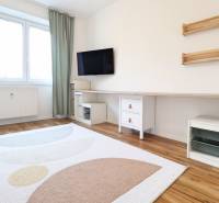 A room in a 3-room apartment with a television, white furniture, and a wooden decor floor.