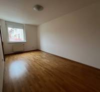An empty room in a 3-room apartment with wooden flooring and a window.