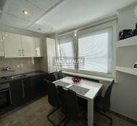 A kitchen in a 2-room apartment with a window, a dining table, and a dark kitchen unit.
