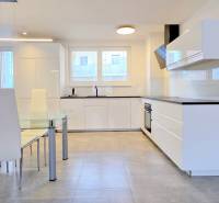 A kitchen in a 2-room apartment with white furniture, a glass table, and a tiled floor.