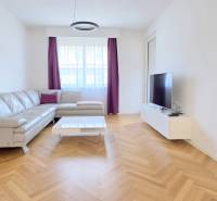 A bright living room with a leather sofa, TV, and wood-patterned flooring in a two-room apartment.