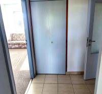 A tiled hallway in a 3-room apartment next to a room with a carpet.