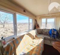 A room with windows overlooking agricultural and forest land and a brown sofa.