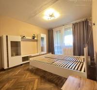 A bedroom in a one-room apartment with a wood-patterned floor and simple furnishings.