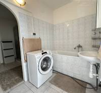 A bathroom in a studio apartment with a washing machine, a sink, and a bathtub on light tiles.