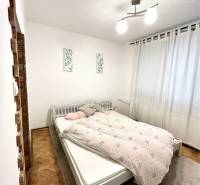 Bedroom with a white bed, light, and a floor with a wooden decor in a 3-room apartment.