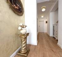 A hallway with a wooden decor floor, a golden stand, and a painting in a family house.