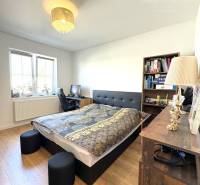 Bedroom in a family house with a bed, wooden decor flooring, window, lamp, and bookshelf.