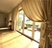 A bright room in a family house, large windows, curtains, and a wooden decor floor.