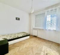 A bright living room in a two-room apartment with a sofa and wood-patterned flooring.