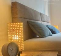 Partial view of a bed in a studio apartment with a lamp and an alarm clock.