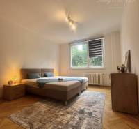 A bright room with a bed, carpet, and wood-patterned flooring in a studio apartment.