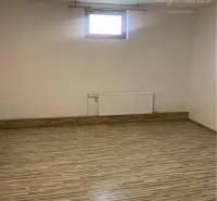 Empty room with wood-patterned flooring, small window, bright walls.