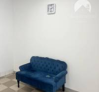A blue sofa with a tiled floor and a wall clock in a commercial space.