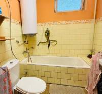 Bathroom with a bathtub and toilet, tiles on the walls, and window ventilation.