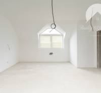 A spacious unfurnished room in a family house with a sloped ceiling and a large window.