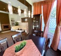 Dining room in a family house with lighting, curtains, and a table with a decorative tablecloth.