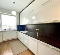 A kitchen in a 2-room apartment with a wood-patterned floor and white furniture.