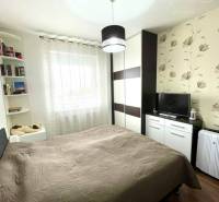 A bedroom in a two-room apartment with a wooden decor floor and floral wallpaper.