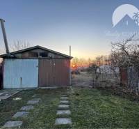 The garden at the family house in Vrakúň with a metal garage and trees, evening sky.