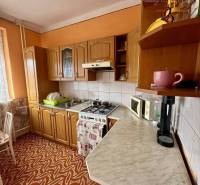 A kitchen in a family house with orange walls, wooden cabinets, and a patterned carpet.
