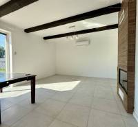 Living room with a fireplace, ceramic floor, and dark ceiling beams in a family house.