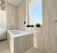 A bathroom with a bathtub and a window in a family house with cream-colored tiles.