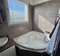 A bathroom corner with a rounded bathtub and a sink in a 4-room apartment.
