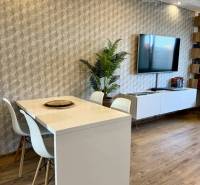 Dining table with white chairs in a 4-room apartment, wooden floor, TV on the wall.