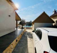 A white car on the driveway, the sun shining on the family house and garden.