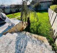 Stone steps lead to the garden, where there are trees and a family house.