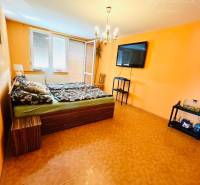 A room in a family house, with orange walls, a chandelier, and a TV on the wall.
