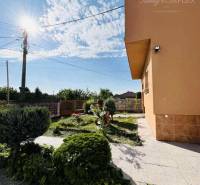 A family house in Okoč with a landscaped garden, sunny weather, sky with clouds.