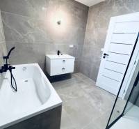 A bathroom with a bathtub and a shower in a family house, tiles with a subtle pattern.