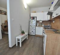 Interior of a 2-room apartment with a kitchen, white furniture, and a floor with a wood decor.