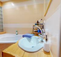 A bathroom with a corner bathtub and a sink in a 2-room apartment, tiles in warm shades.