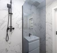 Bathroom with a shower, white marble tiles, and black shower heads in a 3-room apartment.