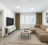 Living room with wood-patterned flooring, sofa, television, and table in a three-room apartment.