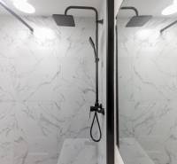 A bathroom with a shower, black fixtures, and marble-patterned tiles in a three-room apartment.