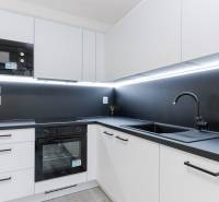 A kitchen in a 3-room apartment with white cabinets, a black countertop, and built-in appliances.